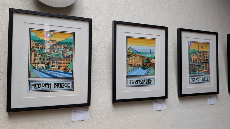 Colourful prints of local heritage buildings hang in a line on a white wall